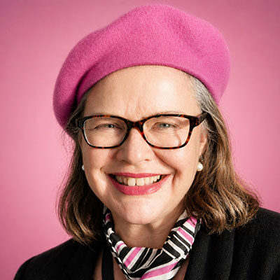 Portrait of Christchurch web designer Michelle Sullivan smiling, wearing a pink beret and glasses against a soft pink background